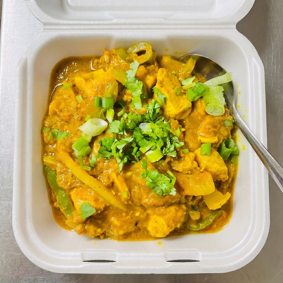 Chicken curry with green peppers, onions, and cilantro in a white takeout container with a spoon.
