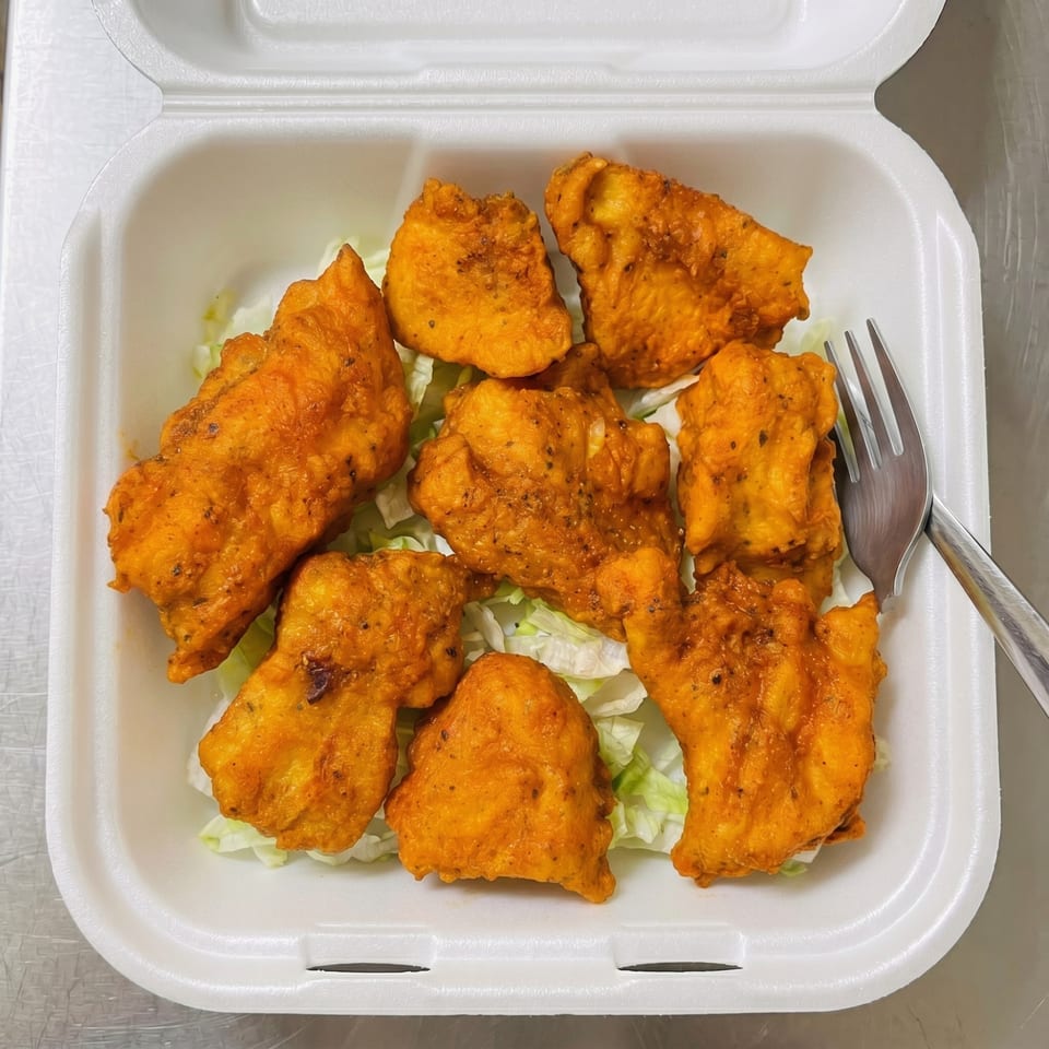 Eight pieces of golden-fried chicken or fish pakora on a bed of shredded lettuce in a white takeout container.