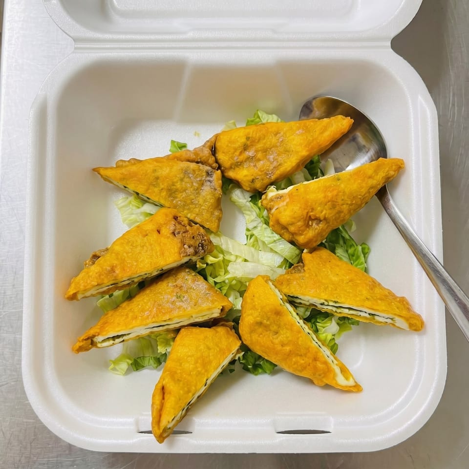 Golden-fried triangular pastries filled with white cheese and green herbs, served on lettuce in a takeout container.