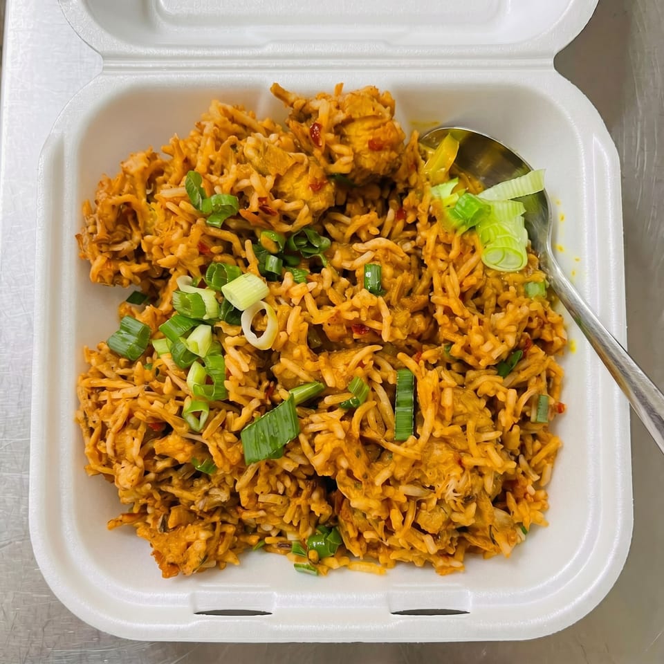 Chicken fried rice with green onions in a white takeout container with a spoon.