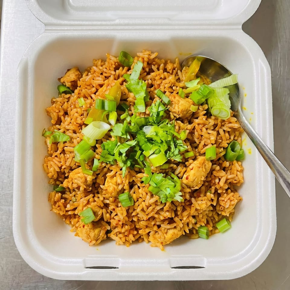 Chicken fried rice with green onions and cilantro in a white takeout container with a spoon.